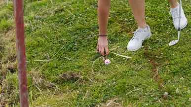 Hand som tar bort gräs runt en golfboll.
