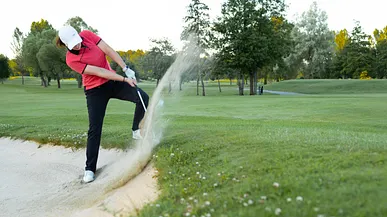 Golfspelare svingar i bunker och skvätter sand.