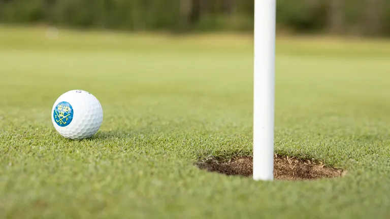 Golfboll med Svenska Golfförbundets logga ligger när hålkoppen på green, flaggan sitter i 