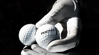 En hand med golfhandske håller två golfbollar.