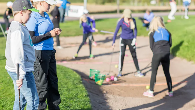 Juniorer och en tränare som tränar på golf.