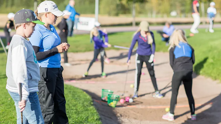Juniorer och en tränare som tränar på golf.
