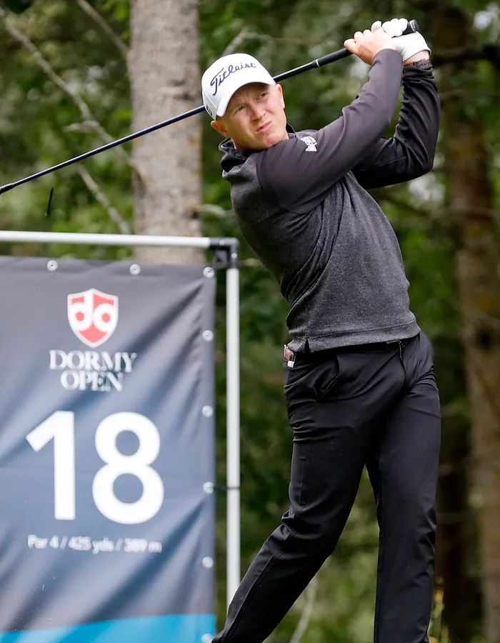 Tourspelare svingar på tee. I bakgrunden en teeskylt med hål 18 och en logga för Dormy Open.